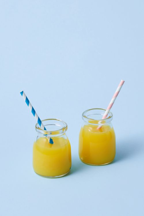 Free Two glass jars of orange juice with striped straws on a pastel blue background. Refreshing and vibrant. Stock Photo