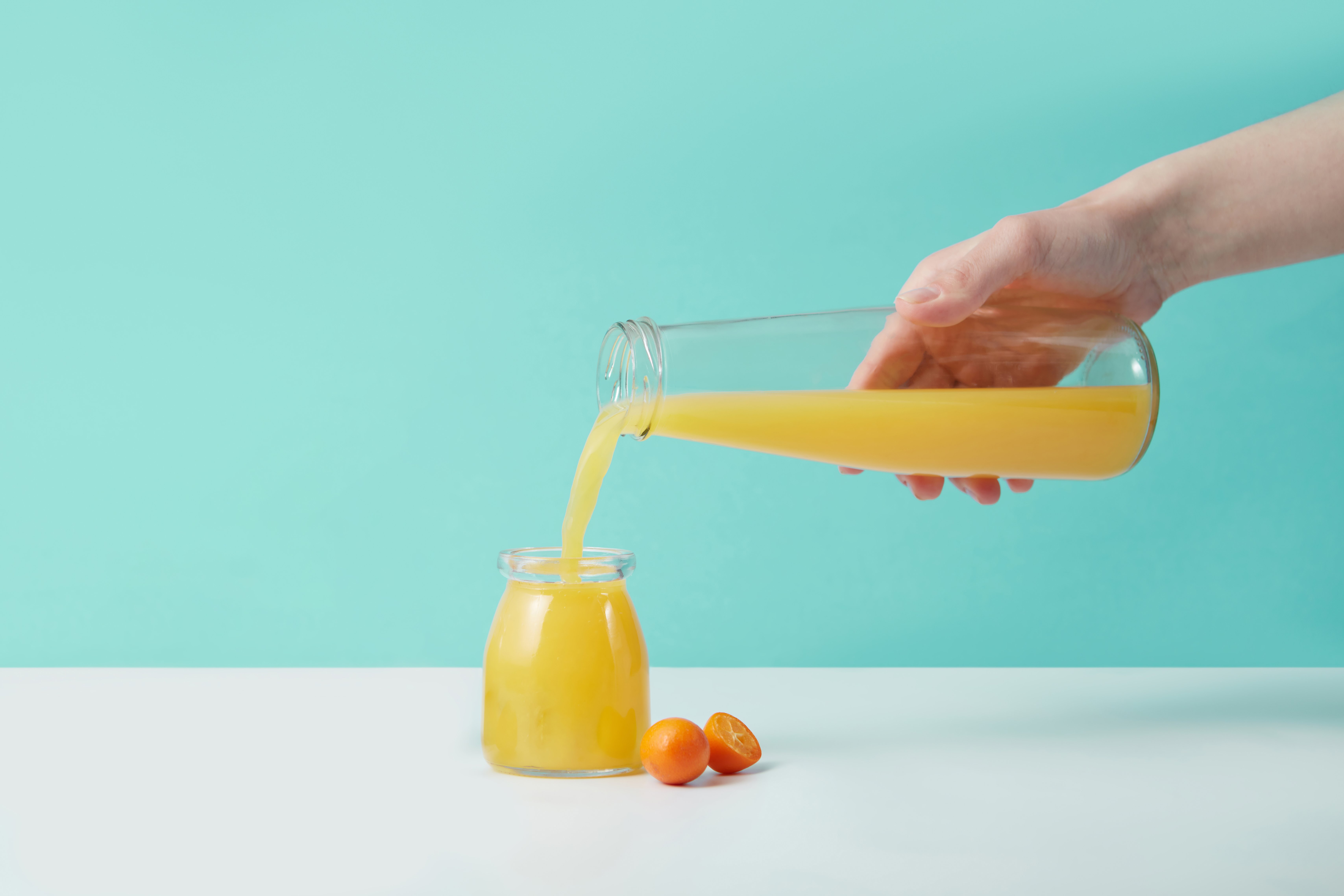 Refreshing orange juice being poured from a glass pitcher into a jar, set against a turquoise background. (Photo: DS stories)