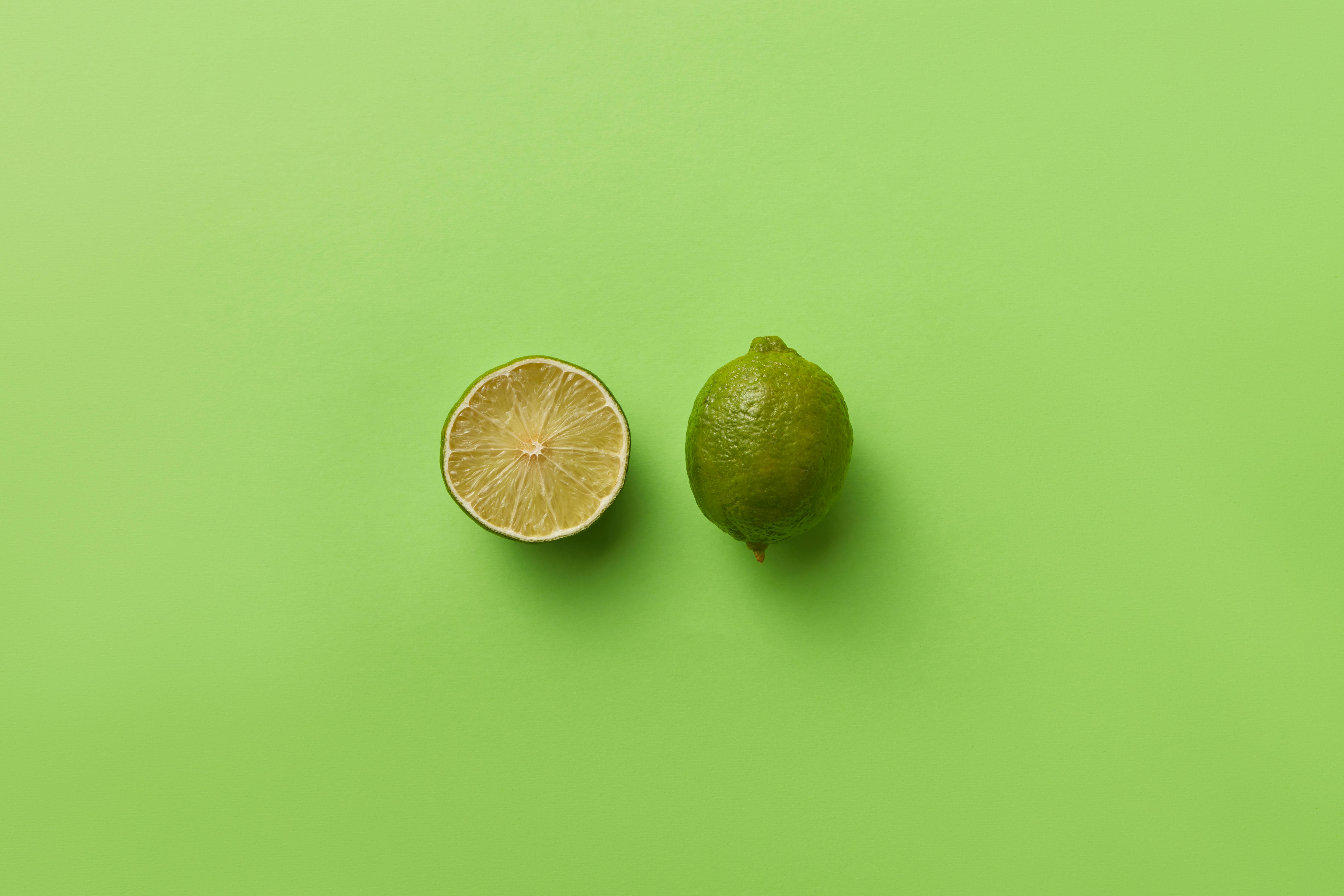 A fresh whole and sliced lime on a vibrant green background with ample copyspace.