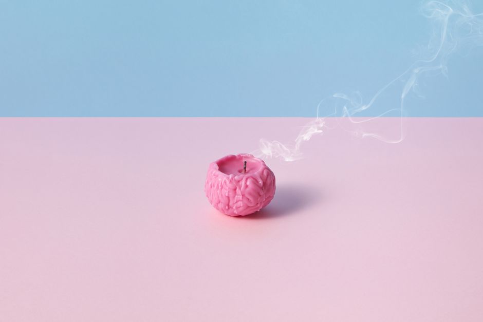 Conceptual image of a pink brain-shaped candle with smoke, on a pastel pink and blue background, symbolizing burnout.