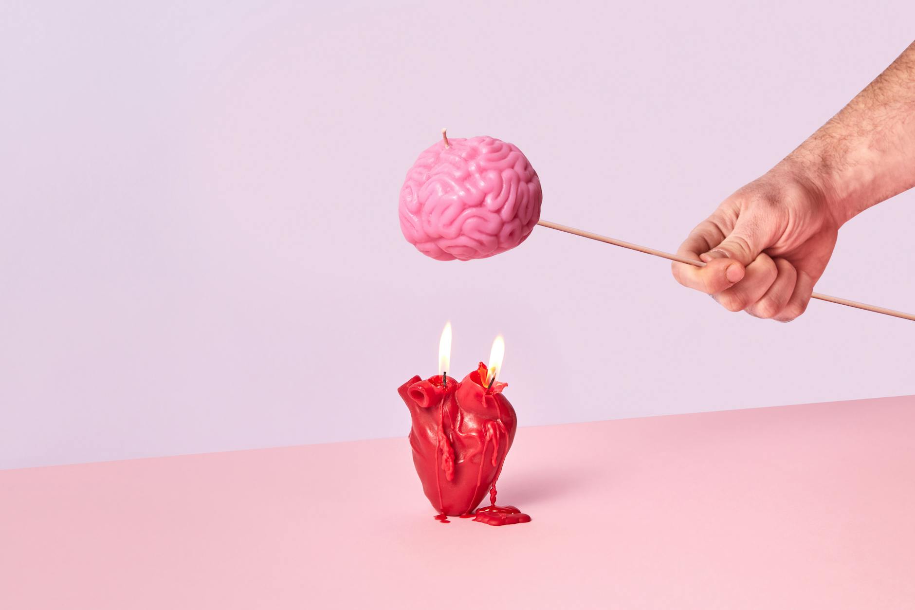 Artistic photo of a hand holding a brain-shaped candle while a heart candle burns below, symbolizing intellect vs emotion.