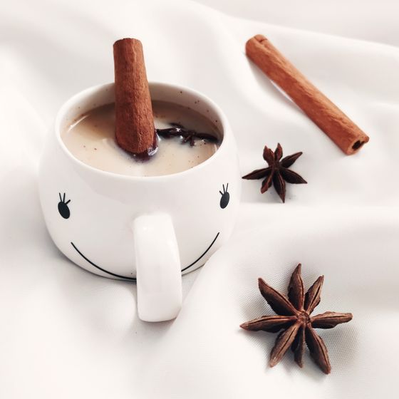 Milky masala chai with a cinnamon stick in a smiling white mug beside star anise