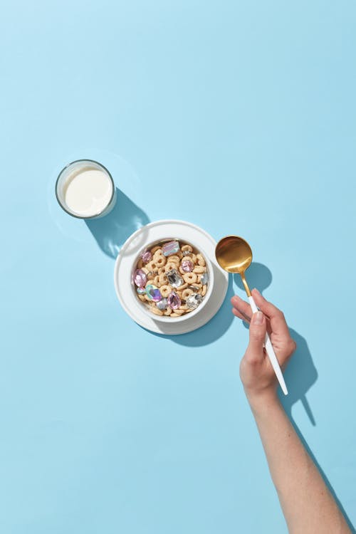 A Hand Holding a Spoon Beside the Bowl of Cereals and a Glass of Milk