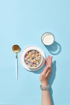 Bright and creative breakfast setup with cereal bowl, milk glass, and hand in view.