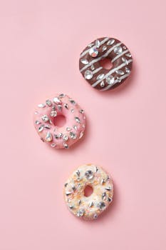 Three decorative donuts embellished with gems on a pastel pink background.