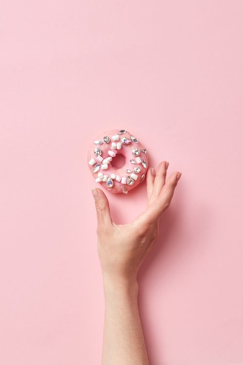 Free A hand reaches for a pink donut topped with marshmallows on a pastel pink background. Stock Photo