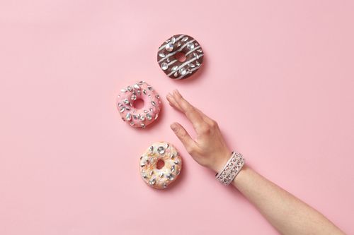 Free Artistic shot of decorated donuts and a hand with a bracelet against a pastel background. Stock Photo