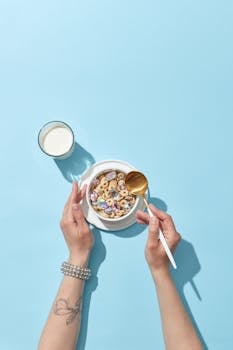 Top view of hands holding a bowl of colorful cereal and milk, set against a blue background.