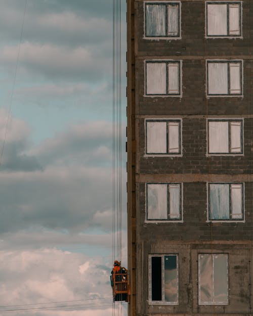 Worker in Crane Lift Ascending along Side of Building