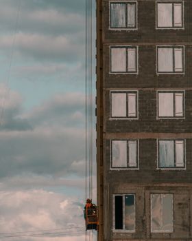 Worker operating crane lift on a high-rise building under cloudy sky