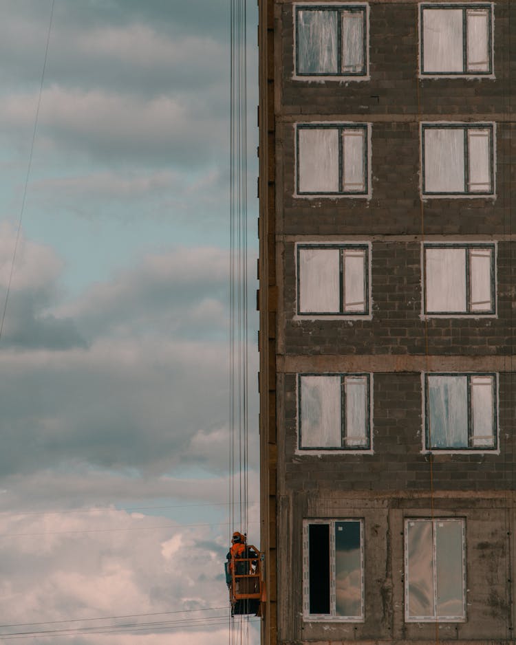 Worker In Crane Lift Ascending Along Side Of Building