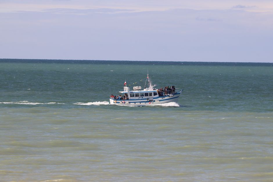 A passenger boat carrying people sails across the open sea under a clear sky, showcasing maritime travel.
