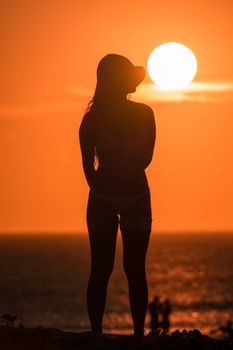 A woman silhouetted against the vibrant sunset over the ocean, creating a dramatic scene.