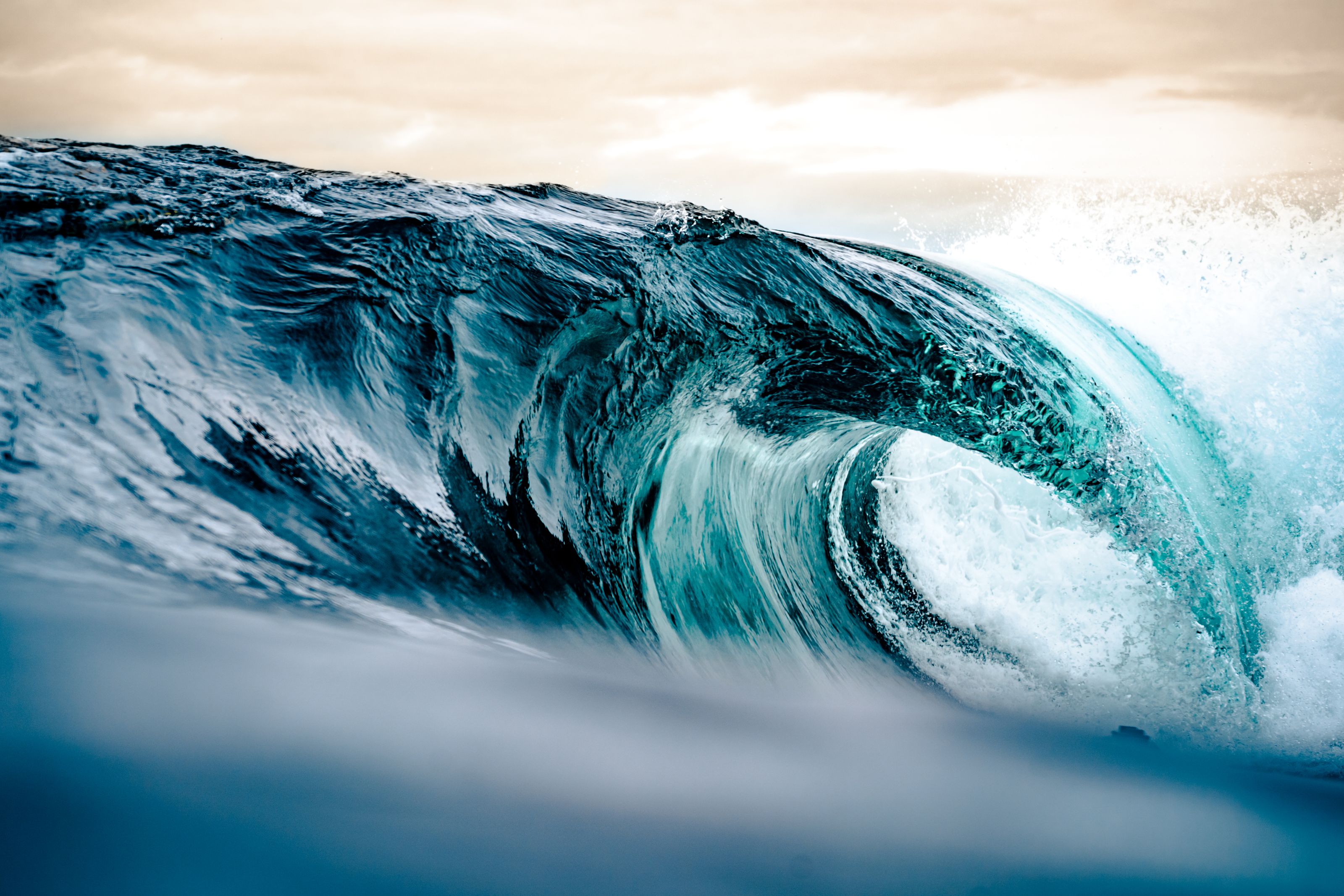 Dramatic ocean wave curling with vibrant turquoise hues at sunrise.