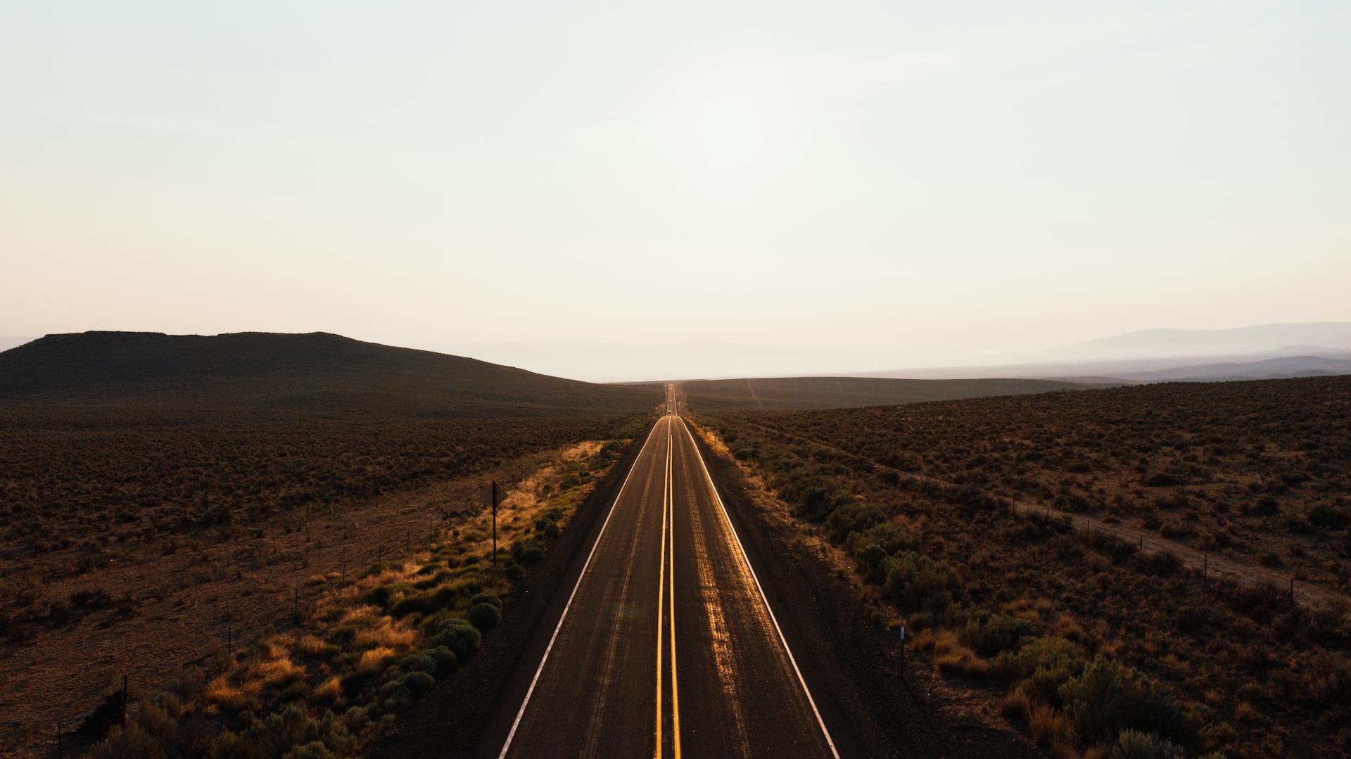 A stunning aerial view of a long desert highway stretching into the distance at sunrise.