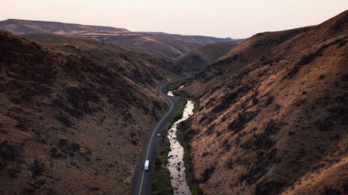 Free Experience the tranquility of a winding road through a picturesque valley surrounded by rugged mountains. Stock Photo