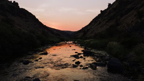 Free A tranquil stream flows through rocky mountains at sunset, capturing nature's beauty. Stock Photo