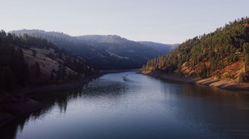 Free A tranquil scene of a river winding between forested mountains during golden hour. Stock Photo