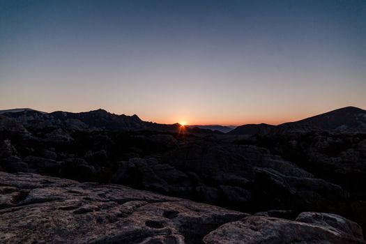 A breathtaking sunset over rugged mountain terrain with a clear sky.