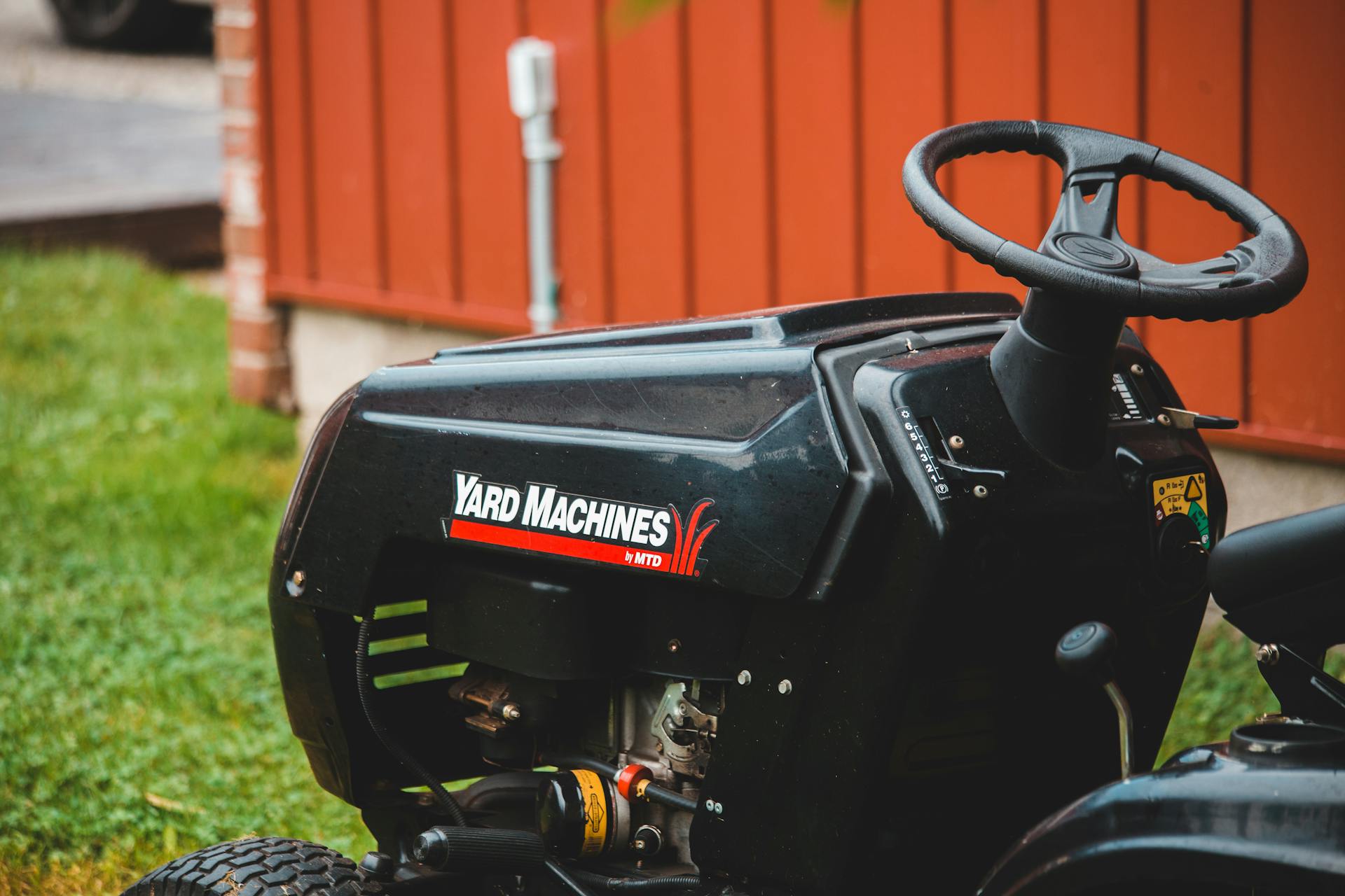 Detailed view of a Yard Machines riding lawn mower parked on grassy lawn beside a red shed.