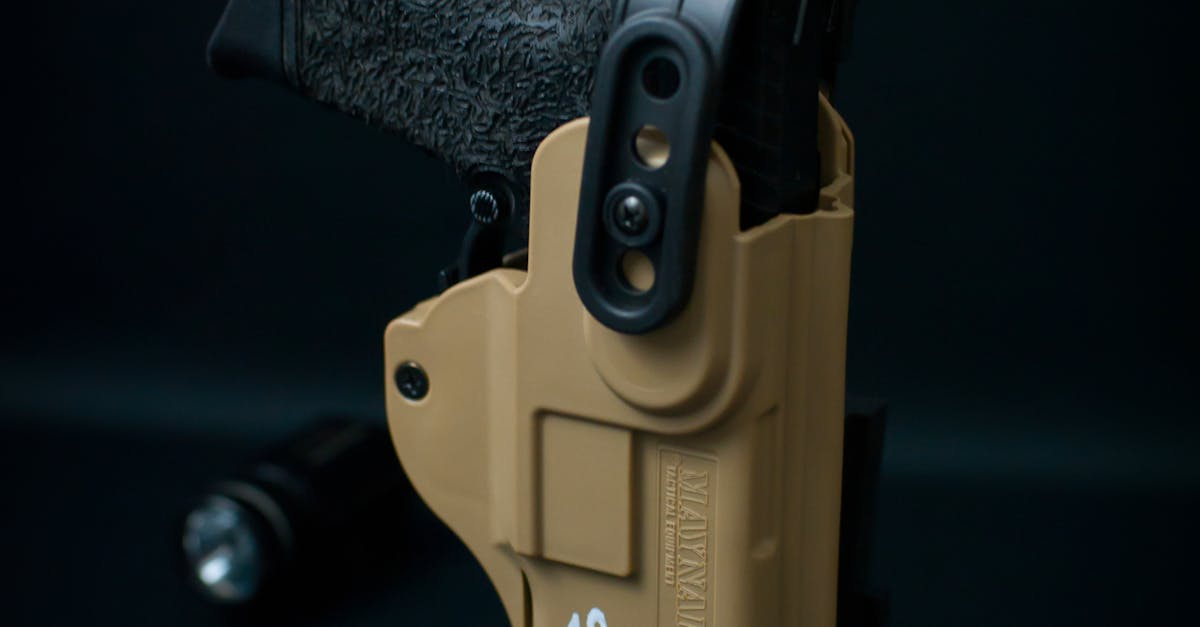 Photo by Dan Galvani Sommavilla Close-up shot of a black handgun secured in a tan holster, against a dark background.