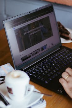 Close-up of hands typing on a laptop with a coffee cup on a wooden table, perfect for lifestyle and technology themes.