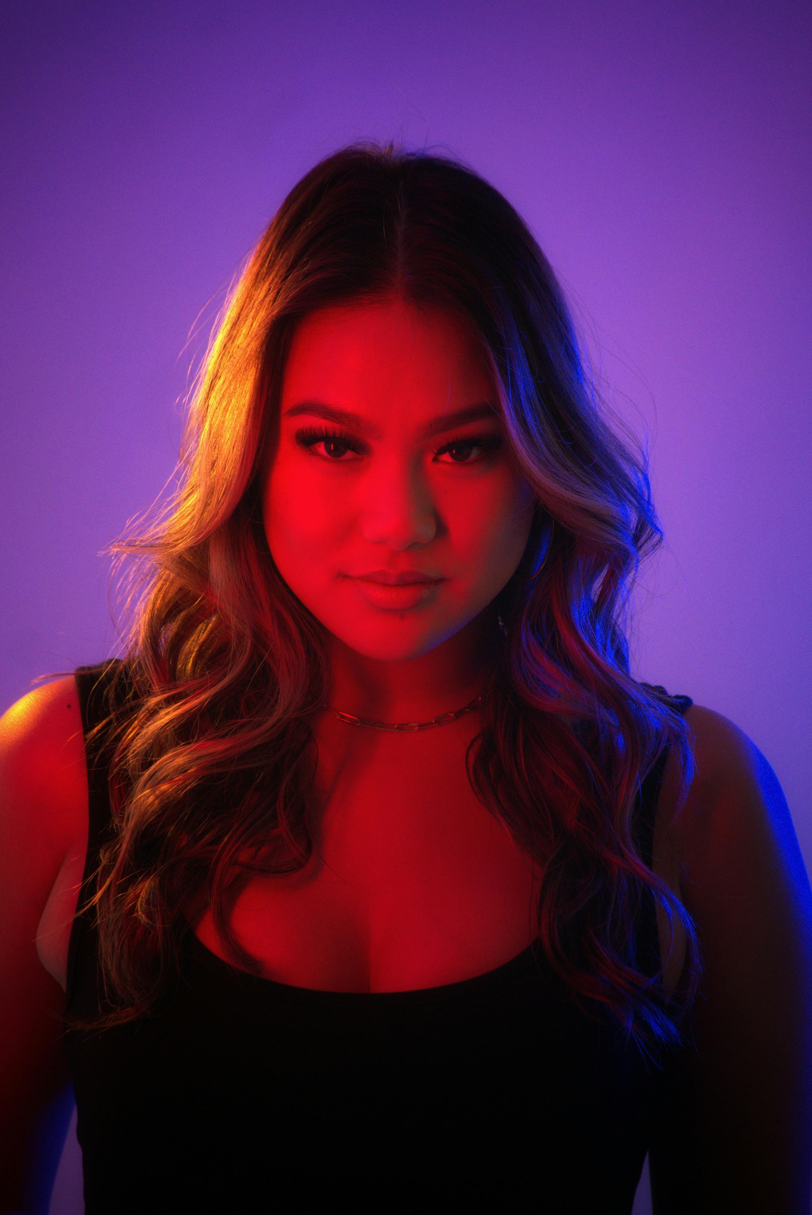 Studio portrait of a woman with dramatic red and blue lighting, curly hair, and confident gaze.
