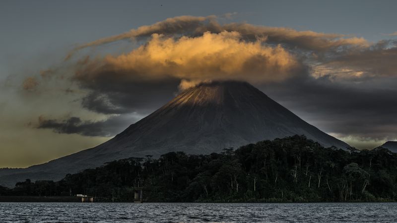 Volcán Arenal con cono completo y nubes doradas al atardecer reflejadas en el lago