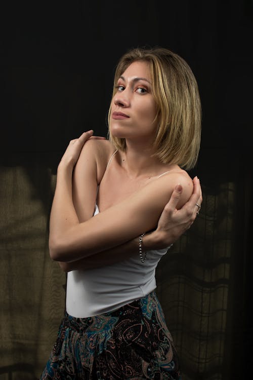 Photo of a Woman in a White Top Posing with Her Hands on Her Shoulders