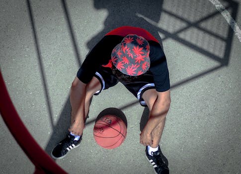 Top view of an athlete sitting with a basketball on a court, wearing a floral bucket hat.