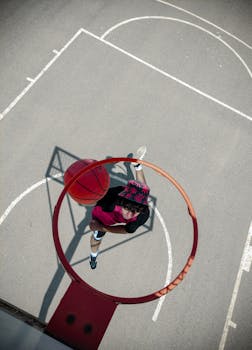 Overhead shot of a person dunking a basketball on an outdoor court in daylight.