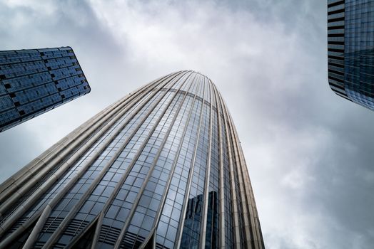 Low angle view of modern skyscrapers with glass facades under a gloomy sky.