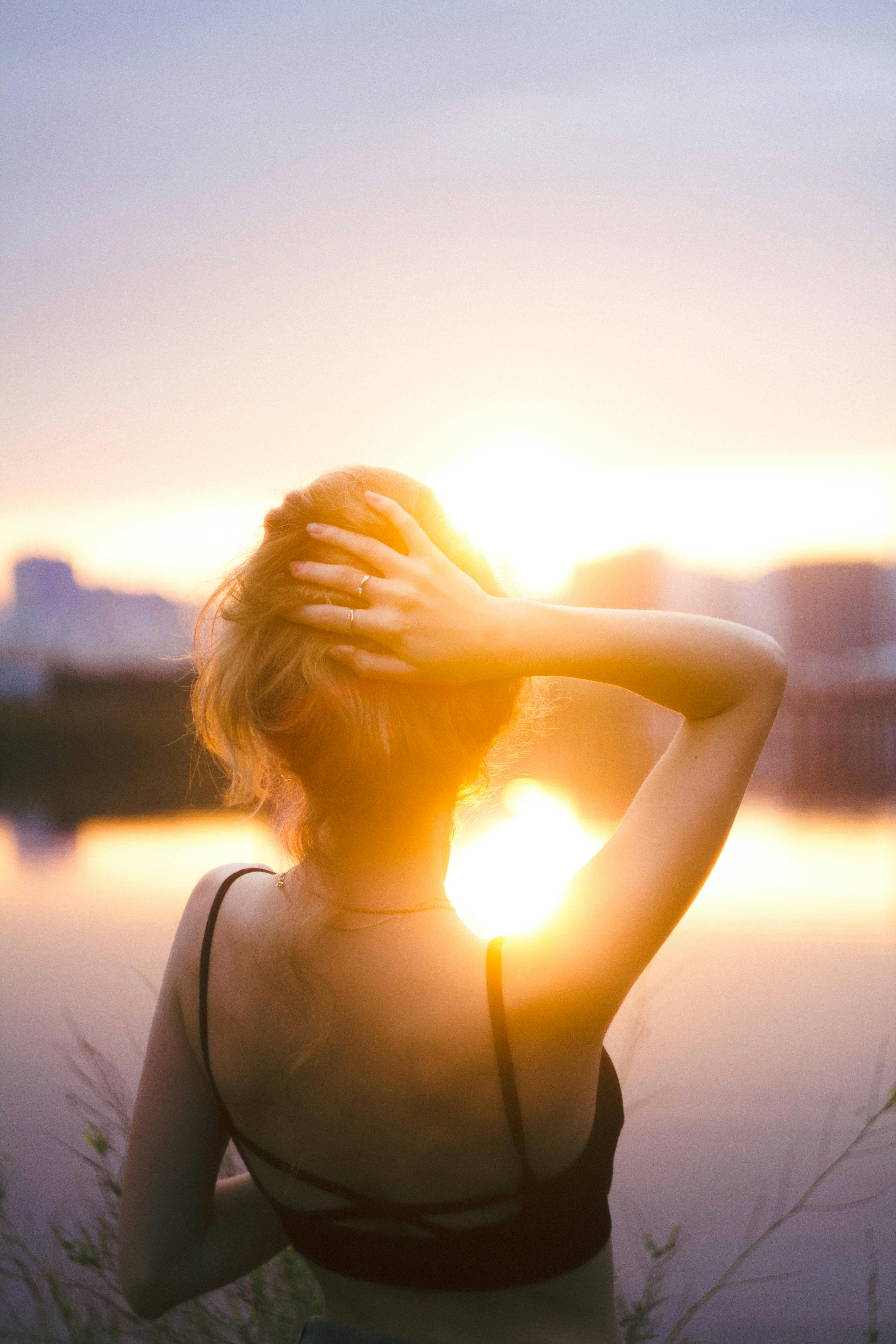 Young woman enjoying a peaceful sunset by a lake, captured in a warm backlit glow.