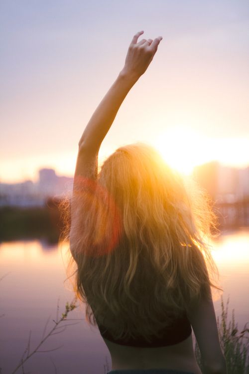 Free Silhouette of a woman raising her hand at sunset by the water, creating a serene and hopeful atmosphere. Stock Photo