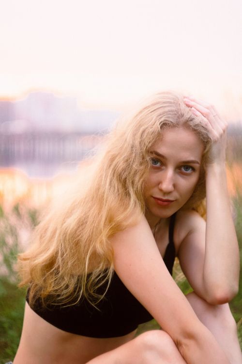 Free Portrait of a blonde woman posing outdoors with a warm backdrop of sunset hues. Stock Photo