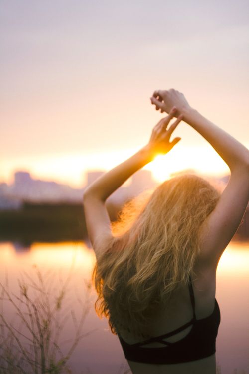 Free A woman raises her arms in relaxation as she enjoys a serene sunset by the lake. Stock Photo