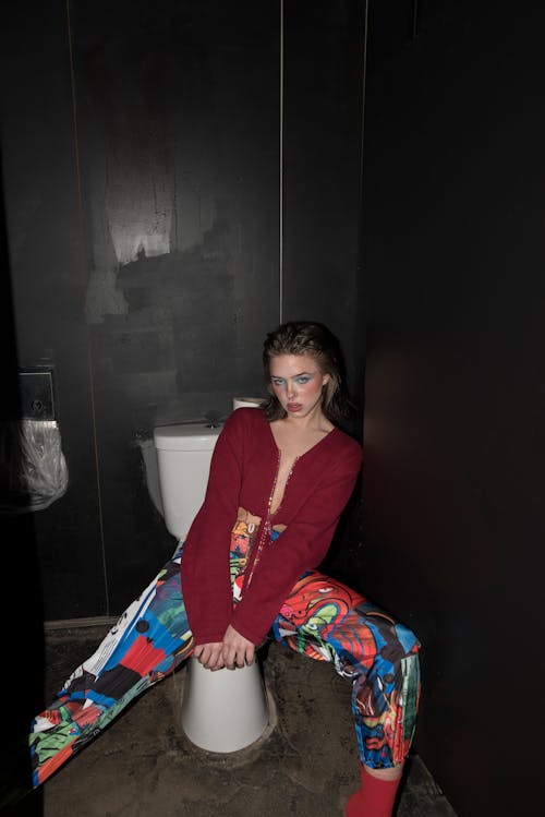 gratis Een Vrouw In Een Rood Shirt Met Lange Mouwen Zittend Op Een Toiletpot Stockfoto