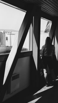 Black and white photo of a woman viewing an airport runway through large windows.