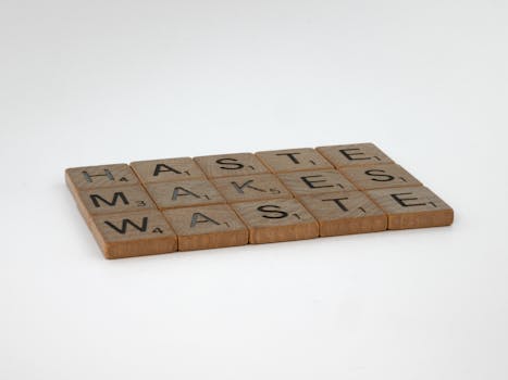 Haste Makes Waste spelled with Scrabble tiles on a white surface, emphasizing patience.