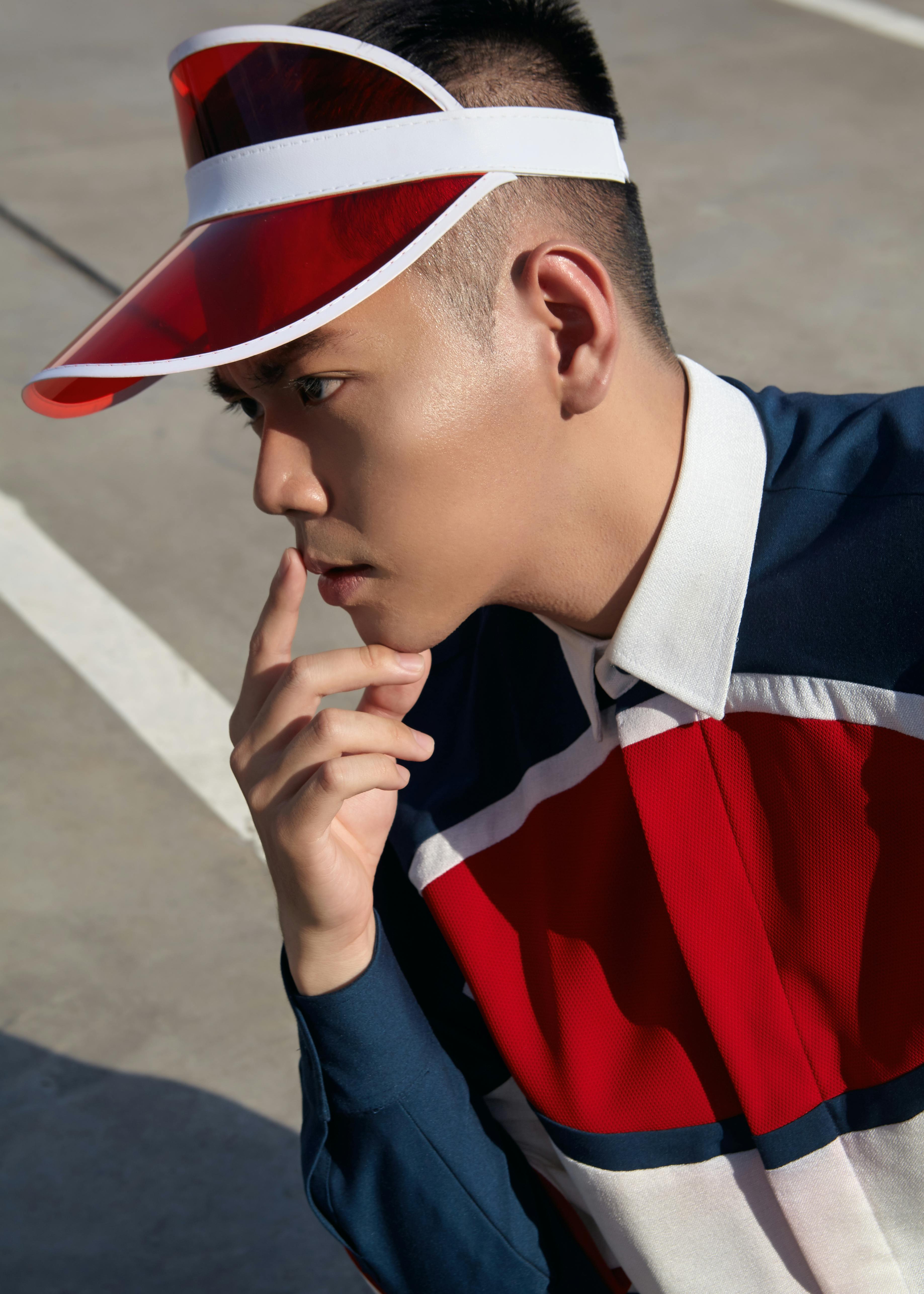 Profile of a fashionable Asian man wearing a red visor and striped shirt outdoors.