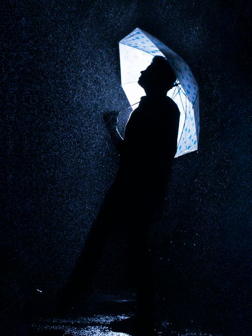 Free A silhouette of a man holding an umbrella under rainfall at night, creating a dramatic effect. Stock Photo