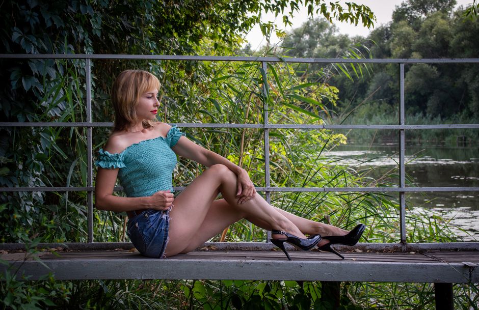 Elegant woman in casual summer attire posing by a serene lakeside, showcasing fashion in nature.