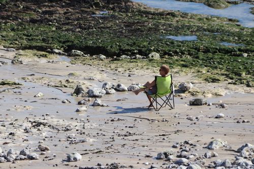 Free A person sitting in a foldable chair enjoys a peaceful moment on a rocky beach. Stock Photo
