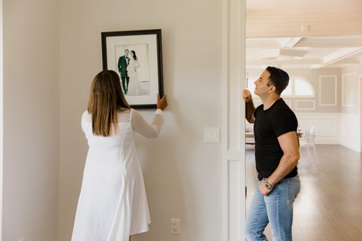 A couple decorates their modern home by hanging a framed photograph on the wall.
