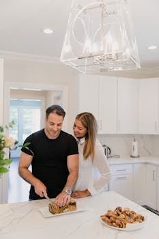 A couple in a modern kitchen slicing homemade bread while sharing a moment of affection.