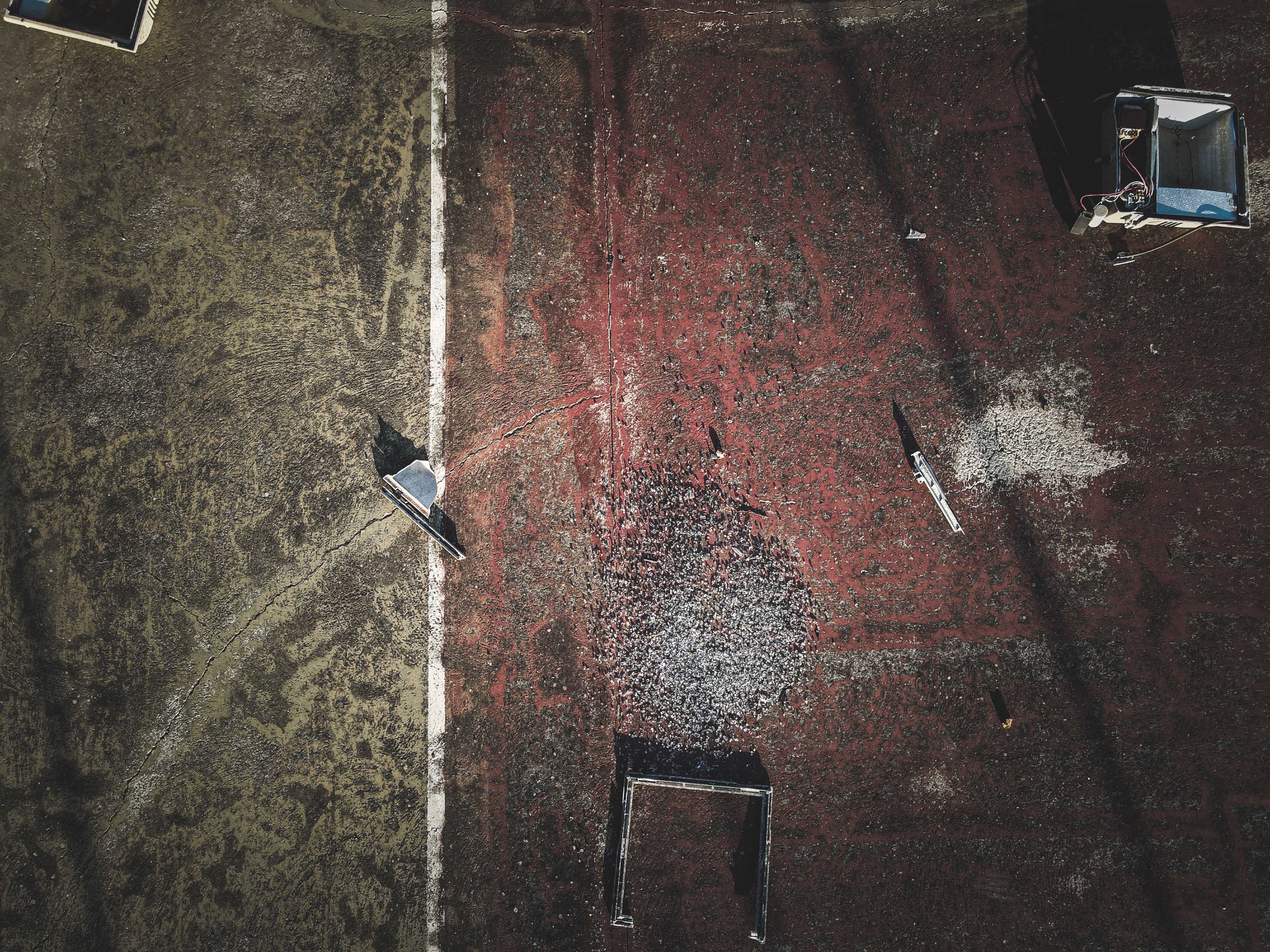 An aerial shot of a decaying, debris-covered tennis court with faded lines and damaged surface. (Photo by Francesco Ungaro on Pexels)