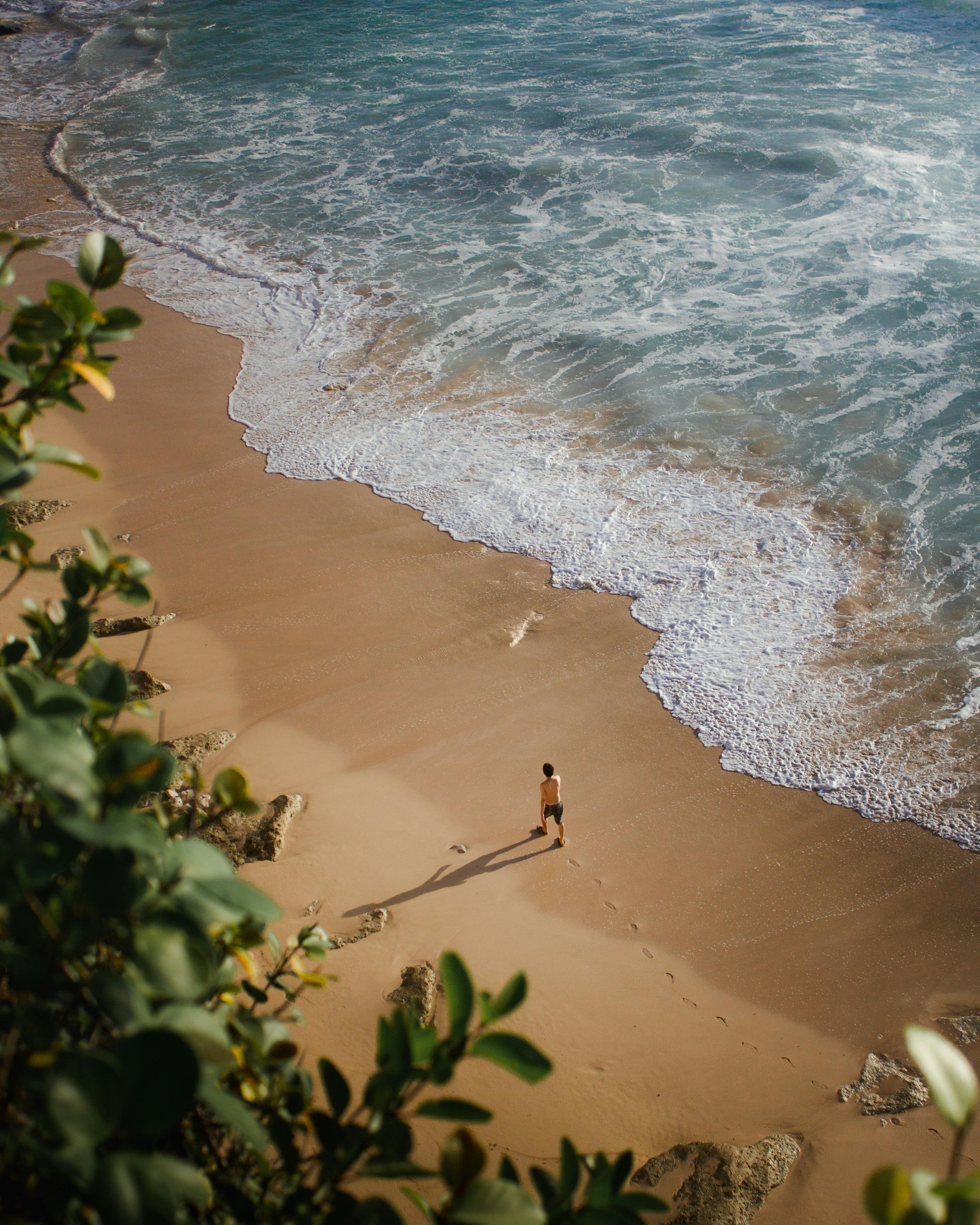 一个成年人沿着原始的巴厘岛海滩散步，海浪从上面拍下