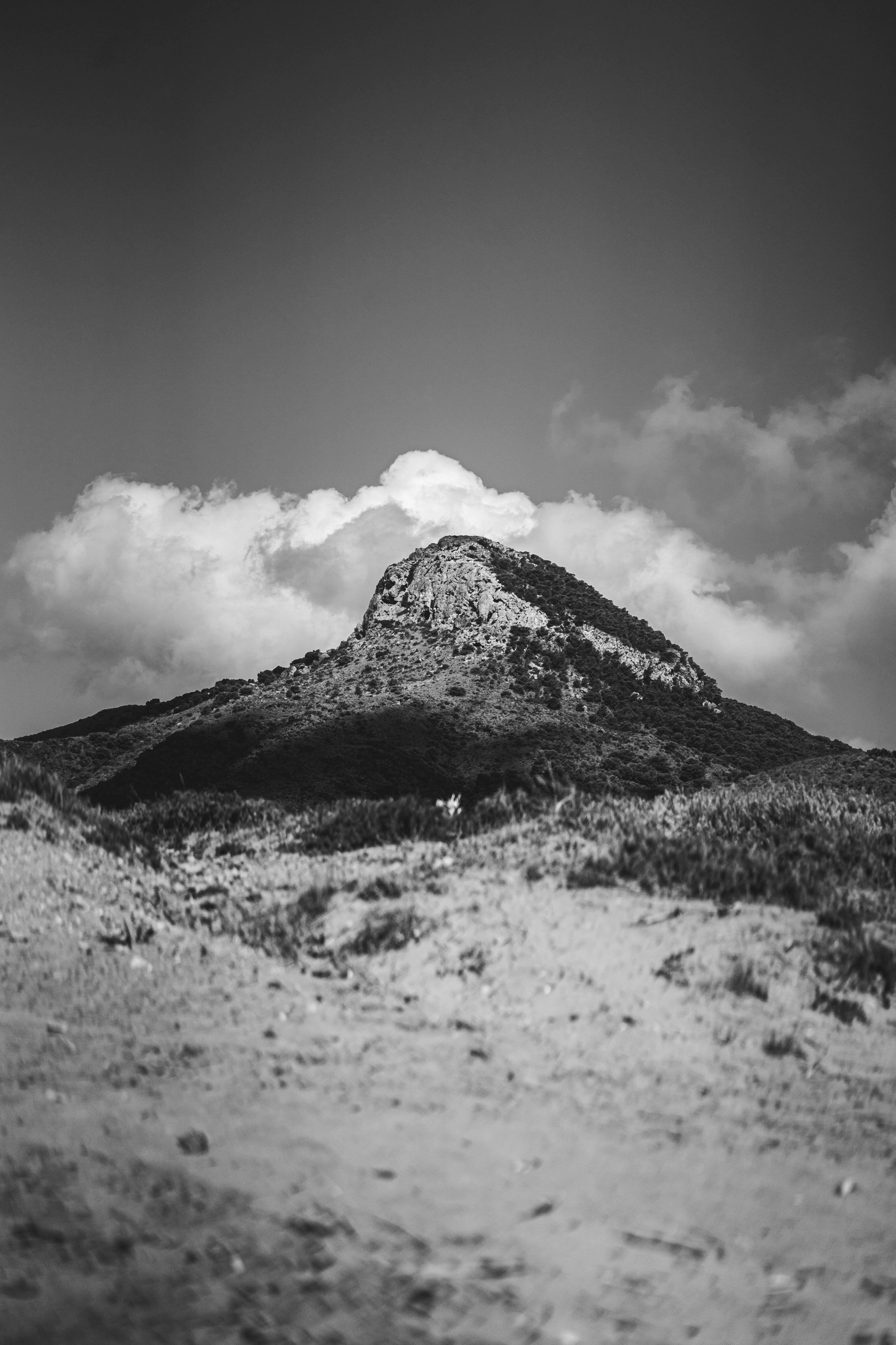 Black and white image of a mountain with a cloudy sky overhead, creating a dramatic effect.