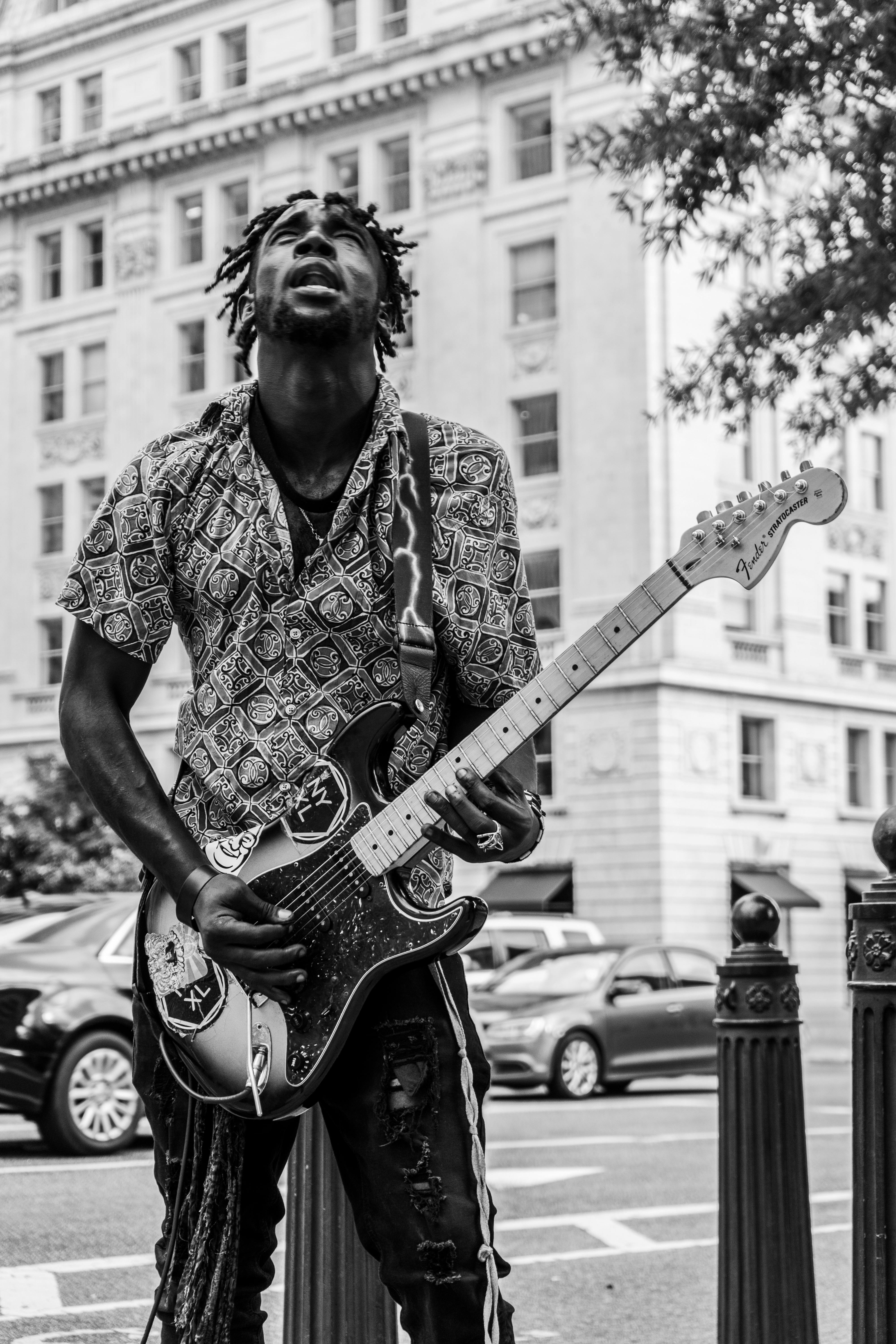 Black and white photo of a street musician with an electric guitar in an urban setting.