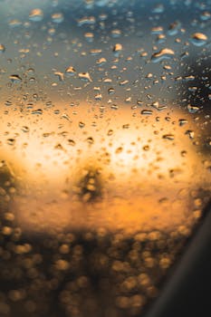 Water droplets on glass with a blurred sunset view, creating an abstract and moody scene.